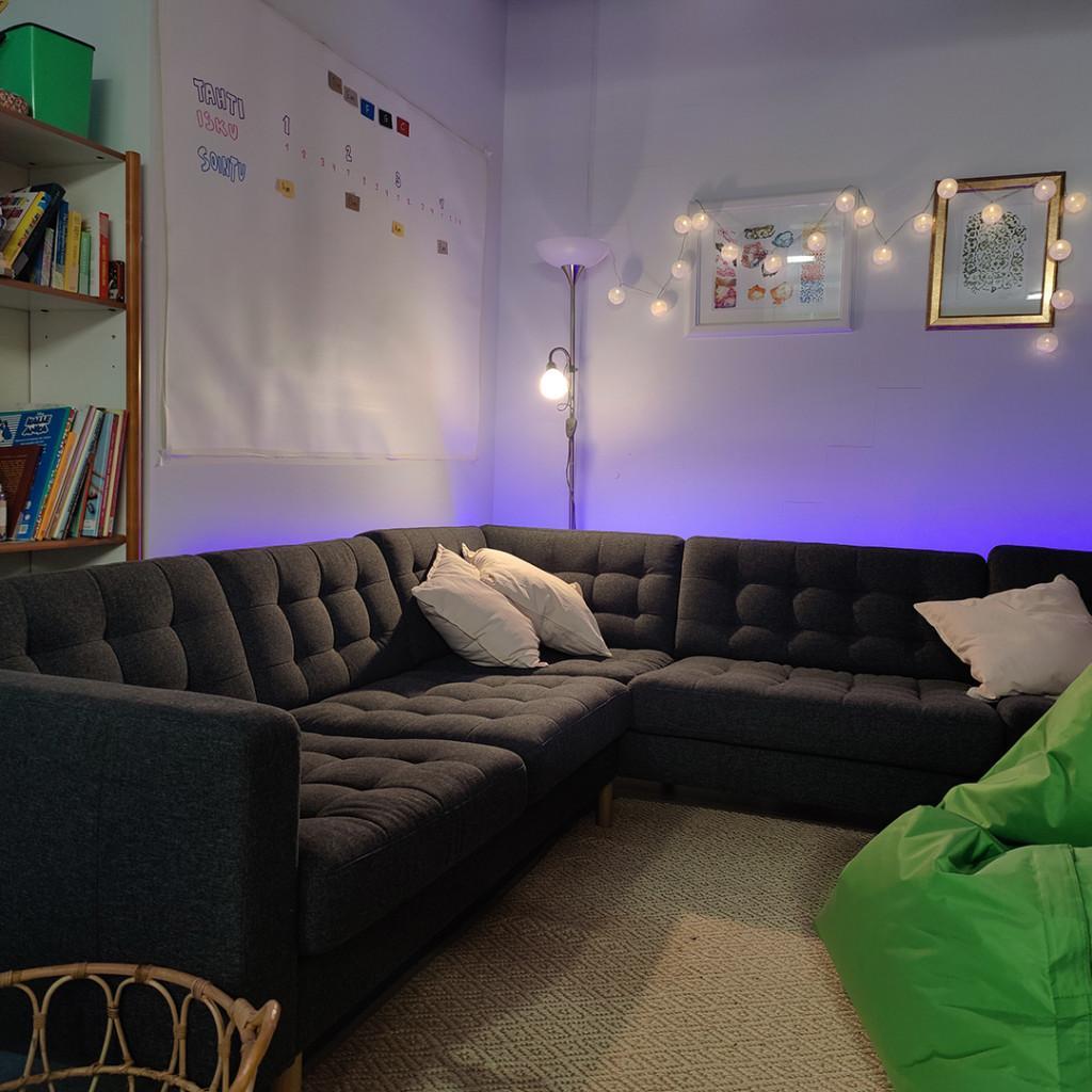 hämärä tila, jossa kirjahylly, sohva, säkkituoli, tauluja seinällä